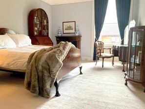 Een slaapkamer met een groot bed, een houten dressoir, een stoel en een spiegel.