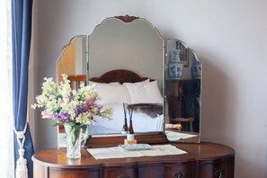A bedroom with a bed, a dresser with a mirror, and a vase of flowers.