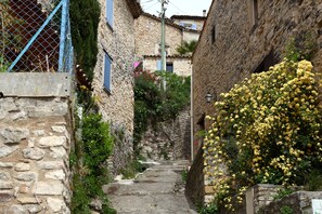 Un étroit sentier pavé de pierres, bordé de bâtiments en pierre rustique, avec un petit jardin aménagé d’un côté.