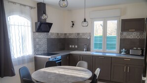 Une cuisine moderne avec un coin repas, comprenant une cuisinière, un évier et une fenêtre donnant sur un espace verdoyant.
