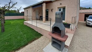 Une maison avec un barbecue en pierre, une terrasse et une voiture garée dans l’allée.