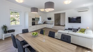 Une cuisine moderne avec des meubles blancs, un coin repas doté d’une table en bois et un salon avec un canapé blanc.