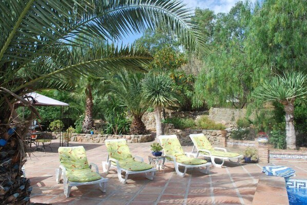 A patio with four white lounge chairs, a small table with a potted plant, and a stone wall in the background. - Large Andalucian Farmhouse, stunning views, pool & gardens,close to Natural Park (El Tropezon, Colmenar)
