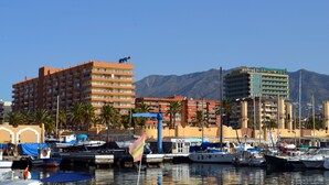 A marina with multiple boats docked, a prominent hotel with balconies, and a mountain range in the background. - APARTMENT NEXT TO THE BEACH AND IN THE CENTER OF FUENGIROLA (Fuengirola)