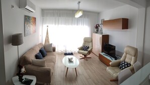 A modern living room with a beige sofa, two armchairs, a glass coffee table, a flat-screen TV, and a decorative tree. - APARTMENT NEXT TO THE BEACH AND IN THE CENTER OF FUENGIROLA (Fuengirola)