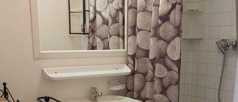 Un baño con lavamanos blanco, un espejo, ducha e inodoro.
