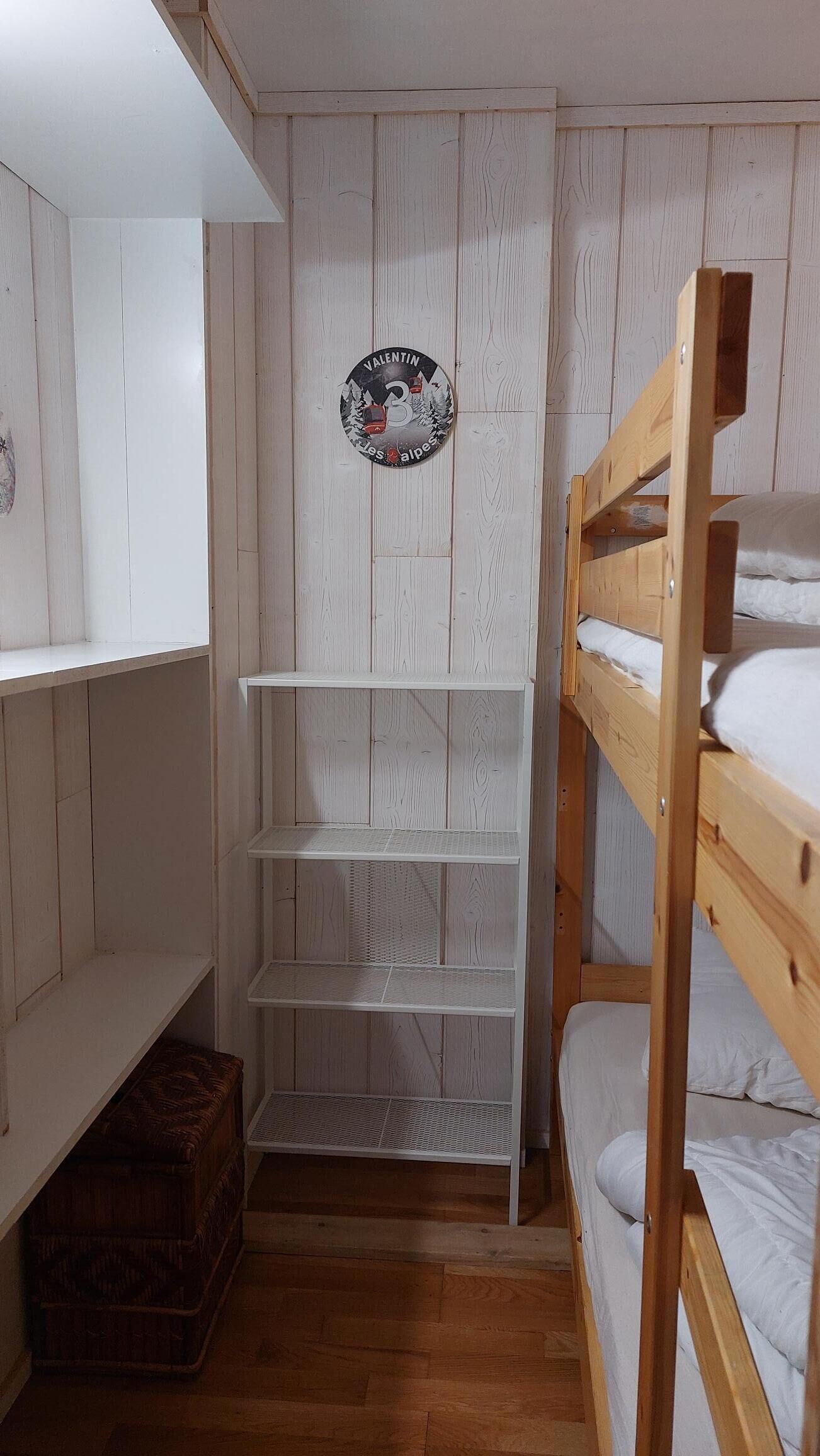 A bunk bed room with a white wooden wall, a shelf unit, and a small chest.