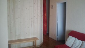 Una habitació amb una banca de fusta, un sofà vermell i una porta que condueix a una altra estança.