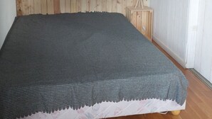 Un dormitori amb un panell de fusta al capçal, un llit amb llençol gris, una tauleta de nit amb una làmpada i terres de fusta.