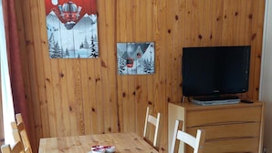 Una habitació amb panells de fusta, una taula de menjador, cadires, un televisor i un armari.