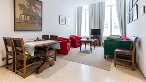 Una sala de estar con una mesa de comedor, sillas rojas, un sofá verde y una televisión.