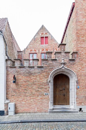 A historic building with a prominent wooden door, brick walls, and a small window with a red shutter. - House of Puebla - Beautiful well-equipped rooms (Brugge)