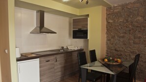 Eine kompakte Küche mit Mikrowelle, Backofen und moderner Schränke. Ein Esstisch mit Stühlen befindet sich in der Nähe einer Steinwand.