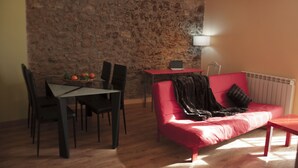Ein Wohnzimmer mit Steinwand, einem roten Sofa, einem Esstisch mit Stühlen und einer Lampe.