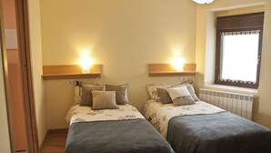 Ein Schlafzimmer mit zwei Betten, jeweils mit Kopfteil, Nachttischlampen und einem Fenster mit Spitze.