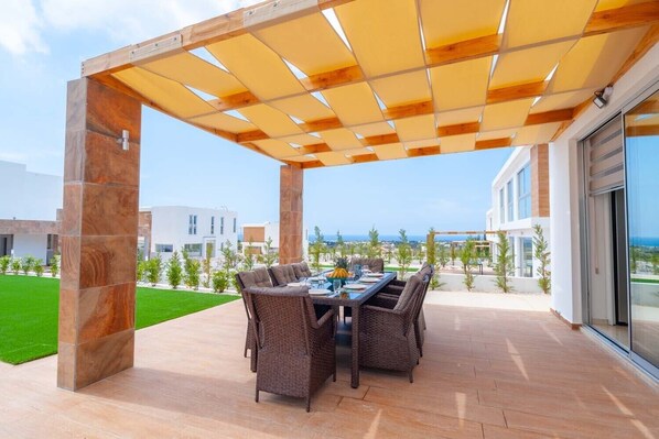 An outdoor patio with a wooden pergola, wicker furniture, and a view of the sea.