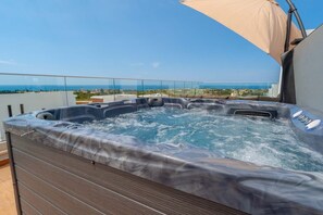 A hot tub on a balcony with a clear view of the ocean and cityscape.