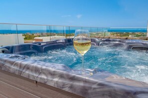 Jacuzzi con una copa de vino blanco en una terraza de madera, con vistas a la costa.