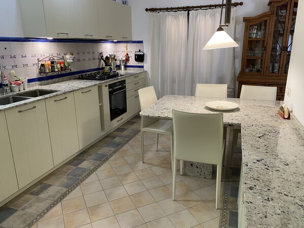 A kitchen with a granite countertop, white cabinets, a dining table with chairs, and a hanging light fixture.