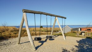 Une balançoire en bois avec deux pneus servant de sièges, placée devant un paysage composé d’une plage et d’une étendue d’eau.