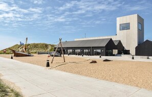 A modern building with a flat roof and large windows, situated on a sandy area with a paved walkway. - Lovely home in Ulfborg with WiFi (Ulfborg)
