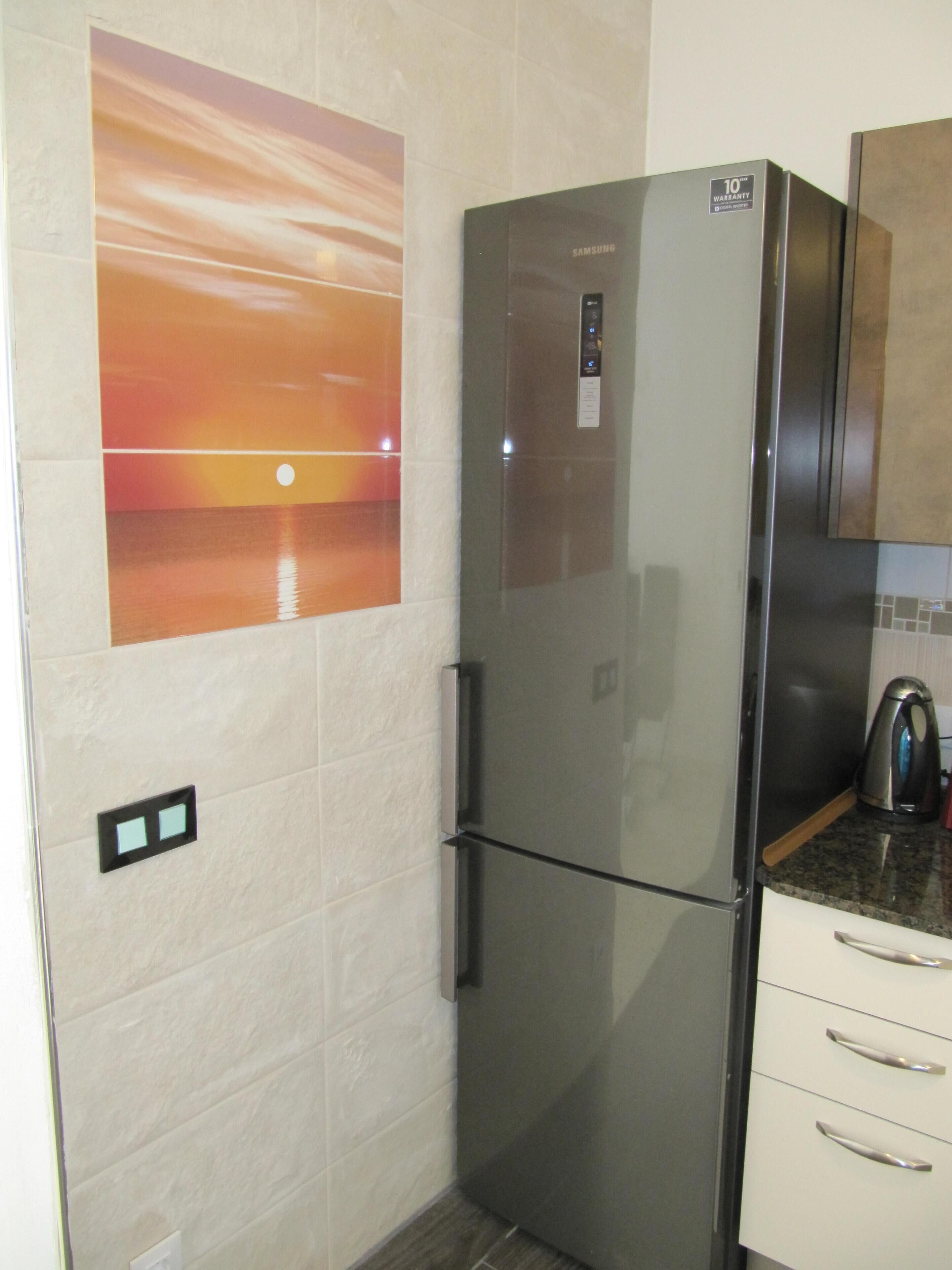 Una cocina moderna con un refrigerador de acero inoxidable, una cafetera y un interruptor de luz en la pared.