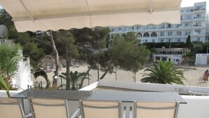 A balcony with a table and chairs overlooking a beach and a building with multiple balconies.