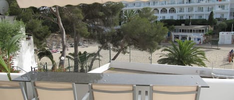 Varanda com mesa e cadeiras, vista para uma praia e um edifício com várias varandas.