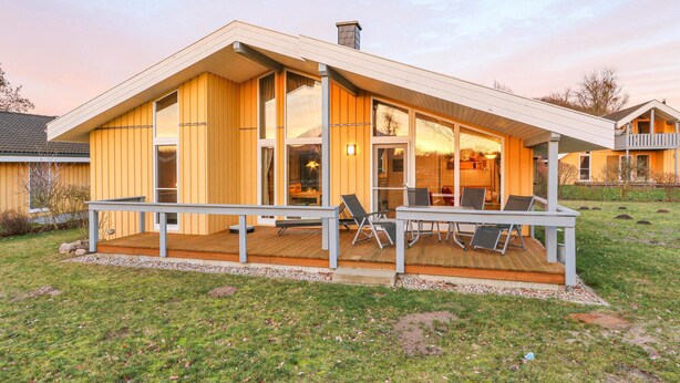 Ett modernt hus med en stor veranda, stora fönster och en skorsten.