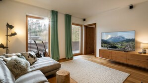 A modern living room with a large flat-screen TV, a wooden cabinet, a sofa, and a small wooden stool. - Apartment Hammerwirt (Fieberbrunn)