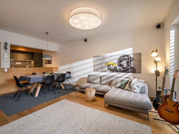 A modern living room with a dining area, a grey sofa, a coffee table, and a guitar.