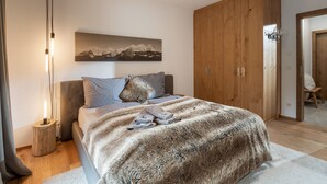 A bedroom with a large bed, a wooden wardrobe, a nightstand, and a wall-mounted light fixture. - Apartment Hammerwirt (Fieberbrunn)