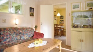Una sala de estar acogedora con un sofá floral, una mesa de centro de madera con bloques decorativos, una planta en maceta y un aparador de vidrio con objetos.
