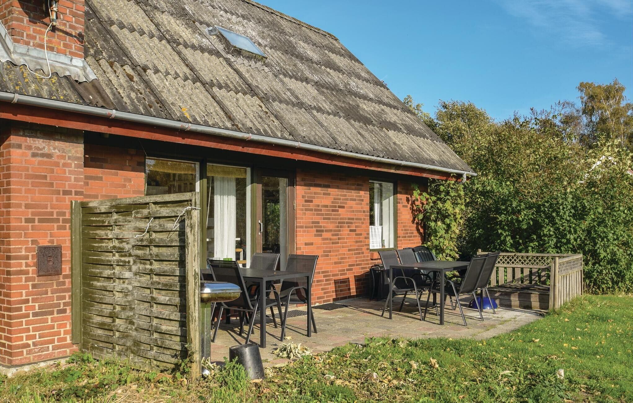 A brick house with a thatched roof, a patio with outdoor furniture, and a wooden gate.