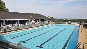 Ein Schwimmbecken mit überdachtem Zuschauerbereich und Blick auf die Landschaft.