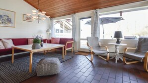 Ein gemütliches Wohnzimmer mit Holzboden, einer Sofagarnitur, einem Couchtisch und einem Essbereich mit Stühlen und Tisch.