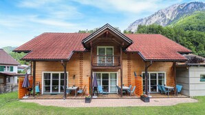 Eine Holzhütte mit rotem Ziegeldach, großen Fenstern und einem Balkon mit Sitzgelegenheit.