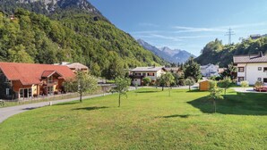 Ein ländliches Dorf mit traditionellen Häusern, einer grünen Wiese und Bergen im Hintergrund.