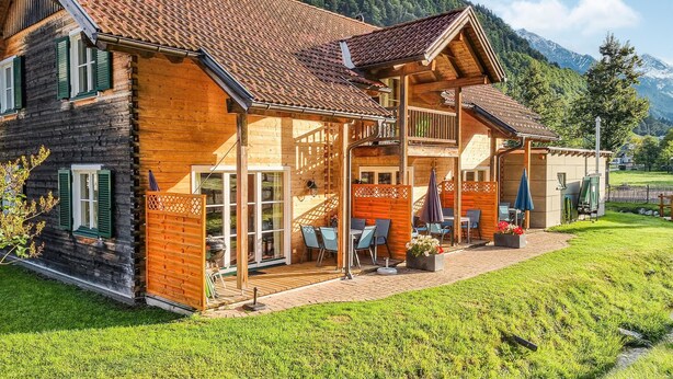 Eine Holzchalet mit Balkon, Sitzgelegenheit im Freien und Blick auf Berge.