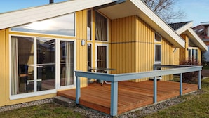 A modern yellow house with large windows, a wooden deck, and a small table. - Stunning home in Rechlin with sauna (Rechlin)
