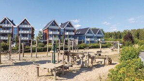 A beachfront property with multiple chalet-style buildings, wooden play structures, and a sandy beach area. - Stunning home in Rechlin with sauna (Rechlin)