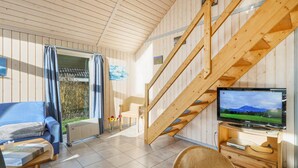 Ein gemütliches Zimmer mit einer Holztreppe, einem blauen Sofa, einem Fernseher und einem kleinen Tisch mit einem Buch.