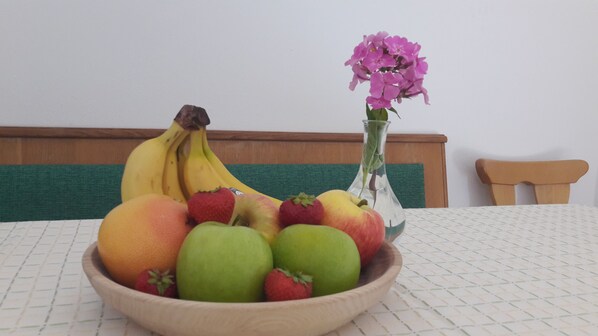 Un cuenco de madera lleno de frutas y un florero con flores sobre una mesa.