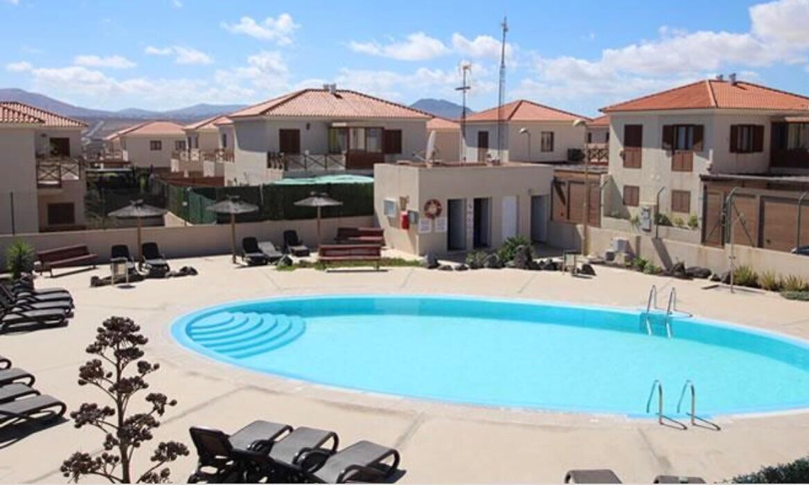 Ein Pool, umgeben von Liegestühlen und einem Gebäude mit rotem Ziegeldach.