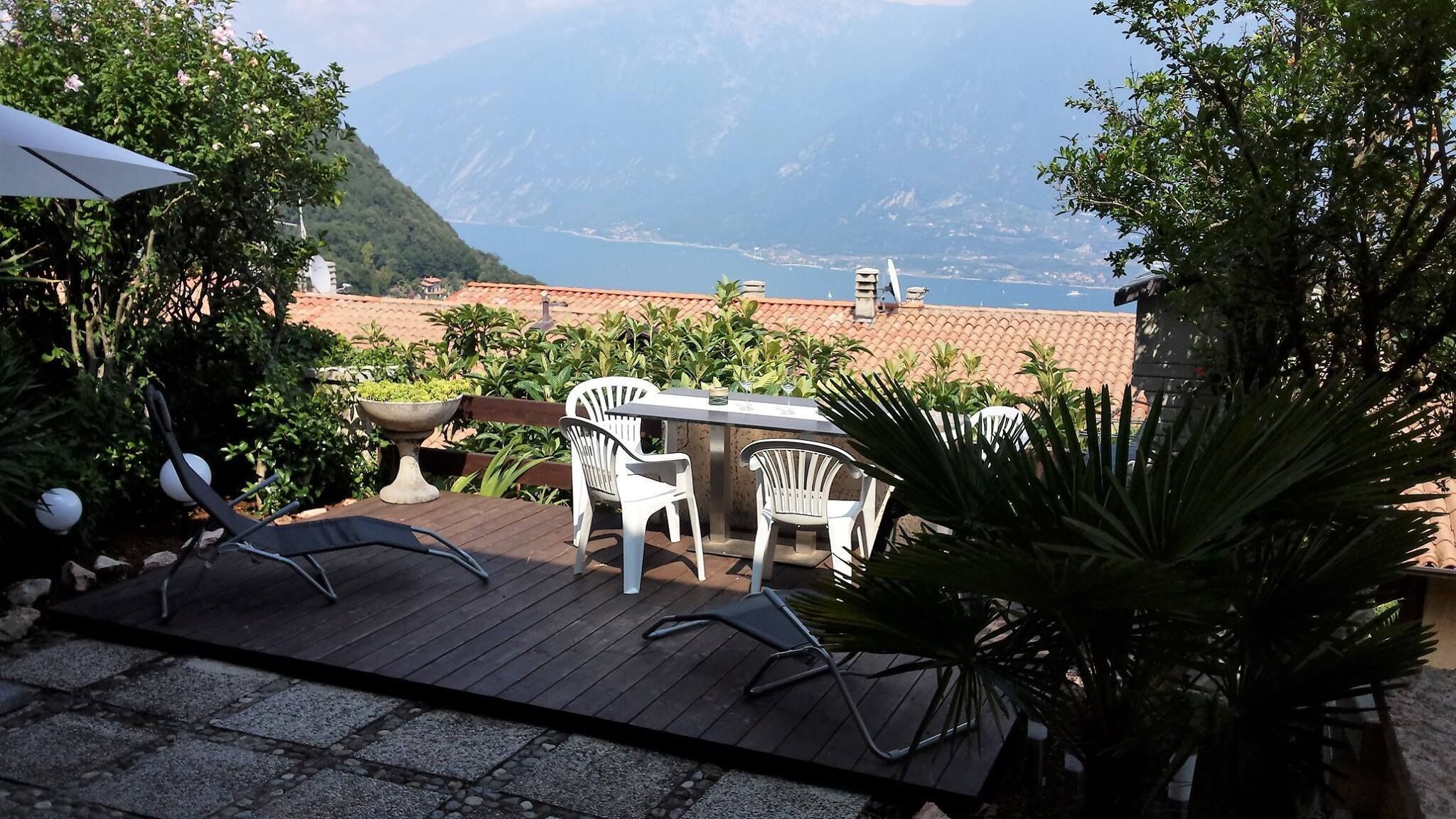 Un patio con mesa y sillas, con vista a un paisaje montañoso y un cuerpo de agua.