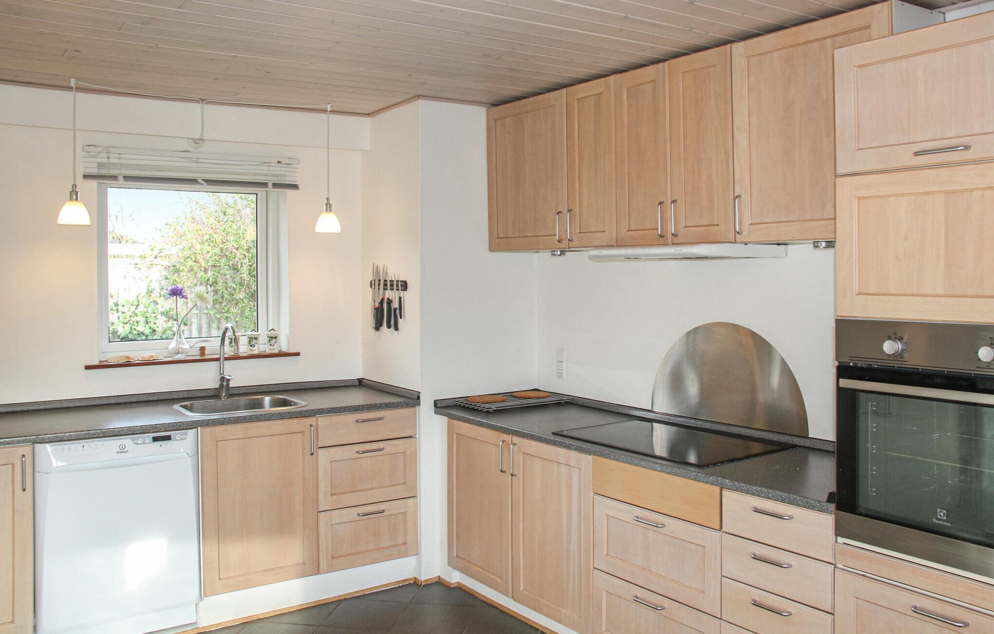 A modern kitchen with wooden cabinets, a stainless steel sink, a built-in oven, and a window with a view of greenery.