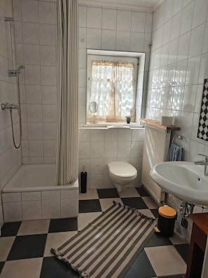 Un baño con bañera, inodoro, lavabo y una ventana con cortina.