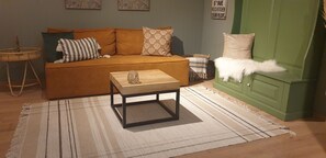 Una sala de estar con un sofá, una mesa de centro, un armario verde y una silla de mimbre.