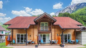Una baita di legno con tetto in tegole rosse, un balcone e una zona patio con posti a sedere all'aperto.