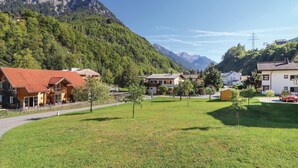 Un villaggio di montagna con case in legno tradizionali, una zona erbosa centrale e montagne scoscese sullo sfondo.
